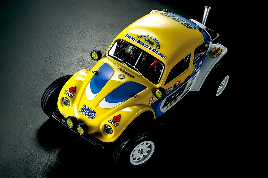 High angle studio shot of a yellow and white Volkswagen Dune Beetle Cross RC buggy on a dark surface.