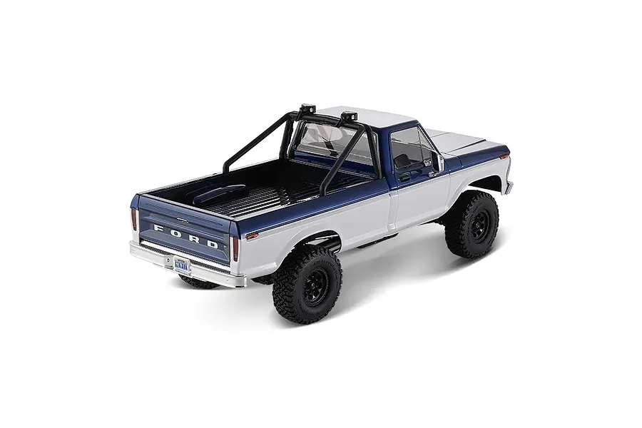 Rear-three-quarter studio shot of the blue and white FMS FCX18 II Ford F-100 RC rock crawler showing truck bed and roll bar.