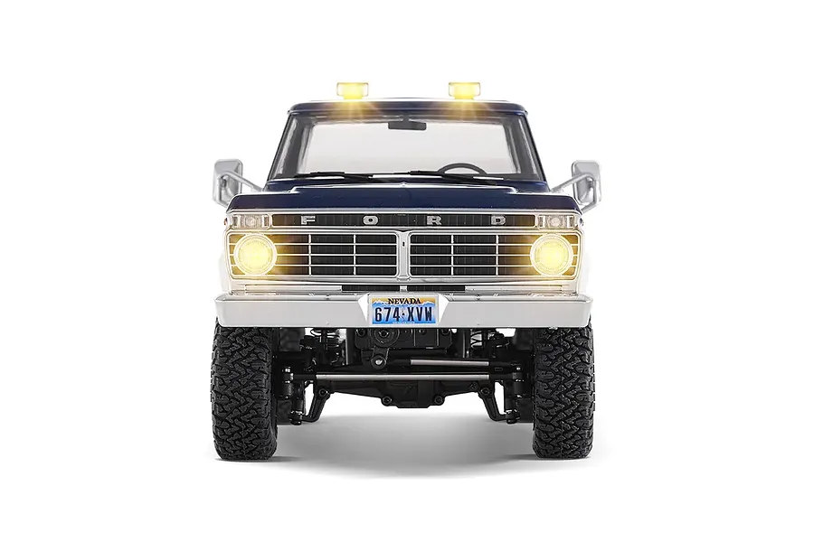Front view of the FMS FCX18 II Ford F-100 RC rock crawler in blue and white with illuminated headlights, roof lights, and a Nevada license plate.