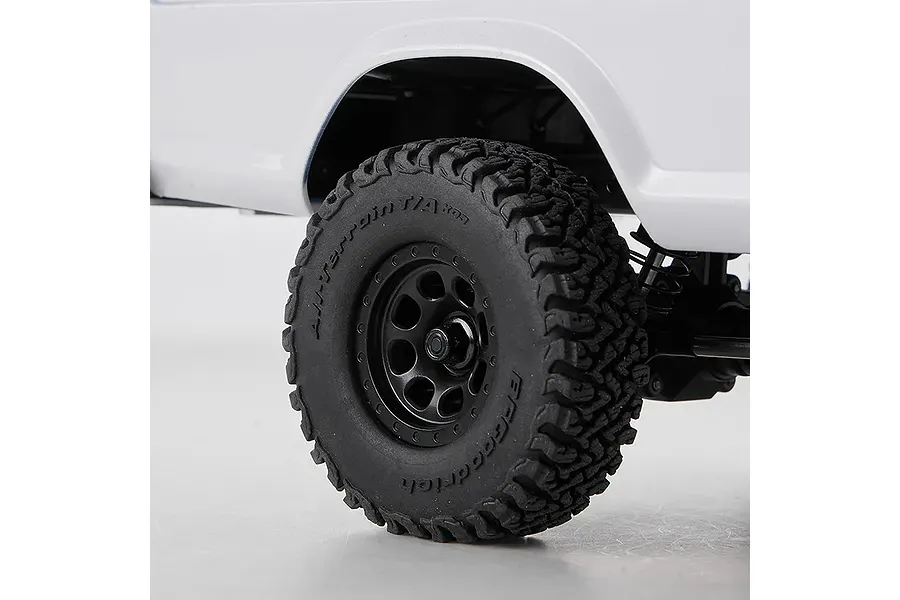 Close-up studio view of the RC rock crawler tire, black wheel, and white fender well on a plain background.