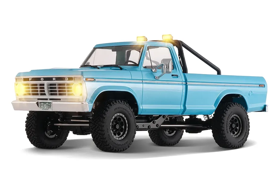 Studio product shot of the FMS FCX18 II Ford F-100 RC Rock Crawler in cerulean blue with working lights lit against a white background.