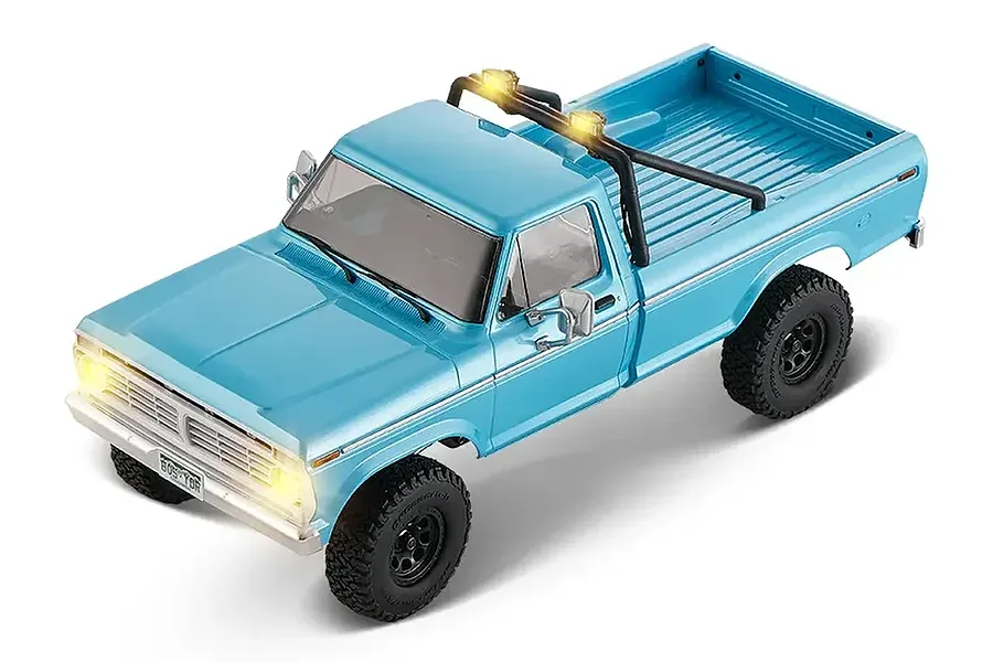 High angle view of a cerulean blue FMS FCX18 Ford F-100 RC rock crawler with lit headlights and roll bar.