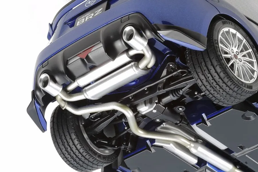 Close-up view of the underside of a blue Tamiya 1/24 scale Subaru BRZ model car, showing the exhaust system, rear suspension, and wheels.