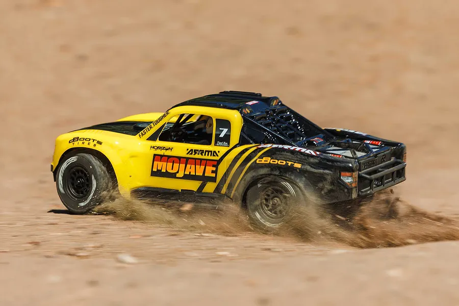 ARRMA Mojave Grom 4X4 RC Short Course Truck driving outdoors on a dirt track, kicking up dust and sand.