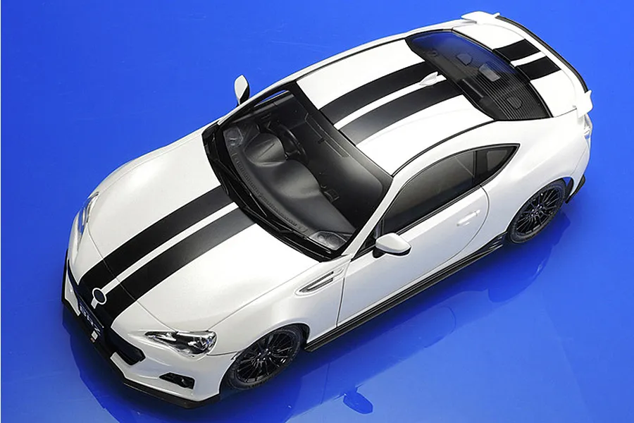 High-angle studio shot of a white Tamiya 1/24 scale Subaru BRZ model car with black racing stripes on a blue background.