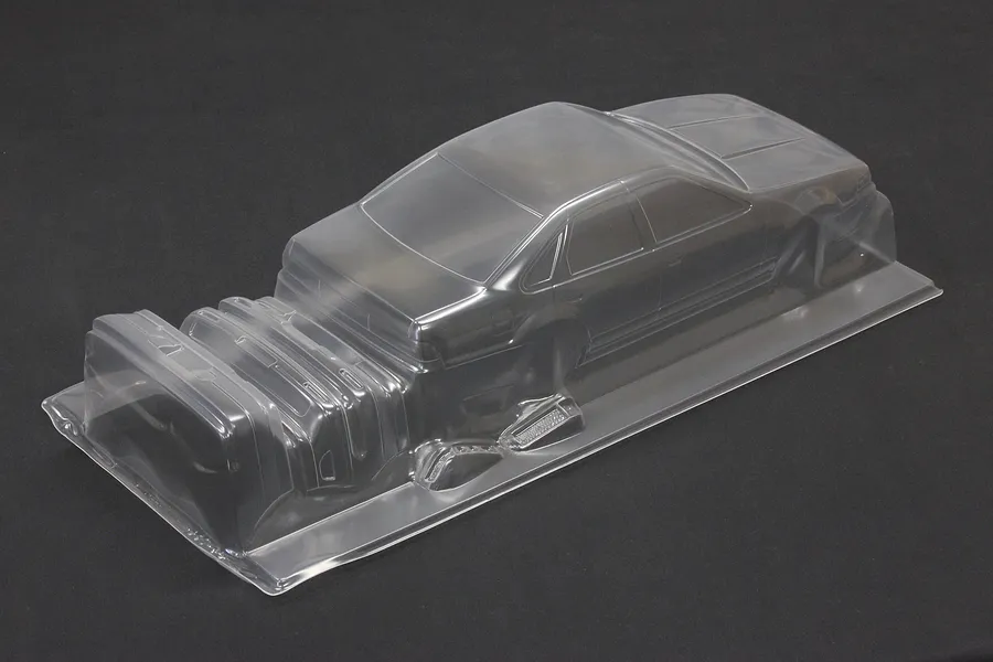 Unpainted clear polycarbonate RC car body shell with additional molded parts in a studio setting against a dark background.