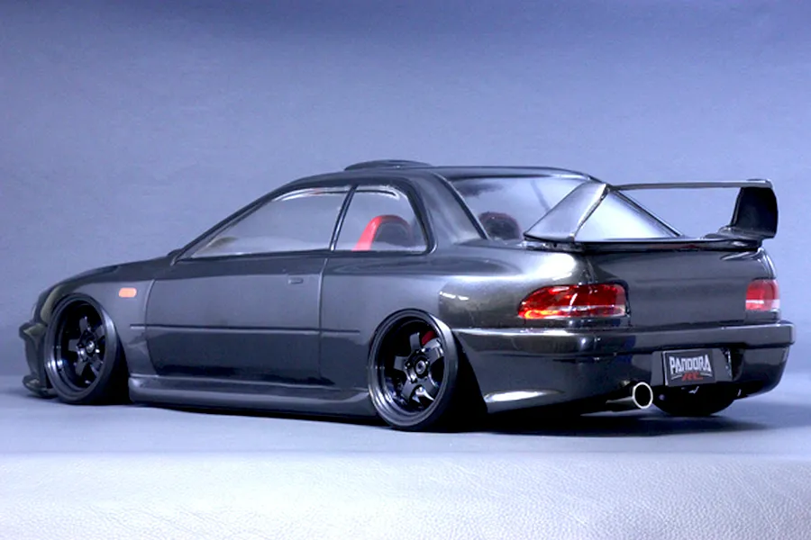 Rear-three-quarter studio view of a grey Subaru Impreza RC drift car body shell with black wheels and a large rear wing.