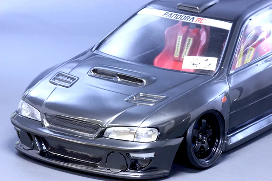 Close-up studio shot of a dark grey Pandora RC Subaru Impreza body shell showing the front end, bonnet vents, and interior seats.