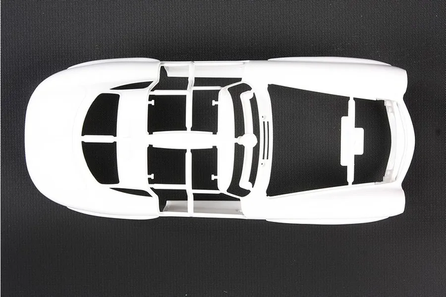 Top-down view of a white plastic model car body shell on a dark textured background.