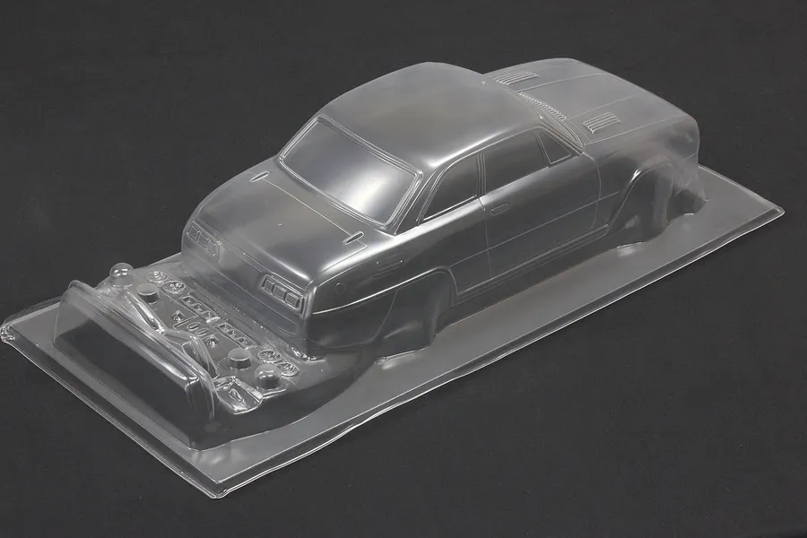 Unpainted clear polycarbonate RC car body shell with additional molded accessory parts on a dark background.