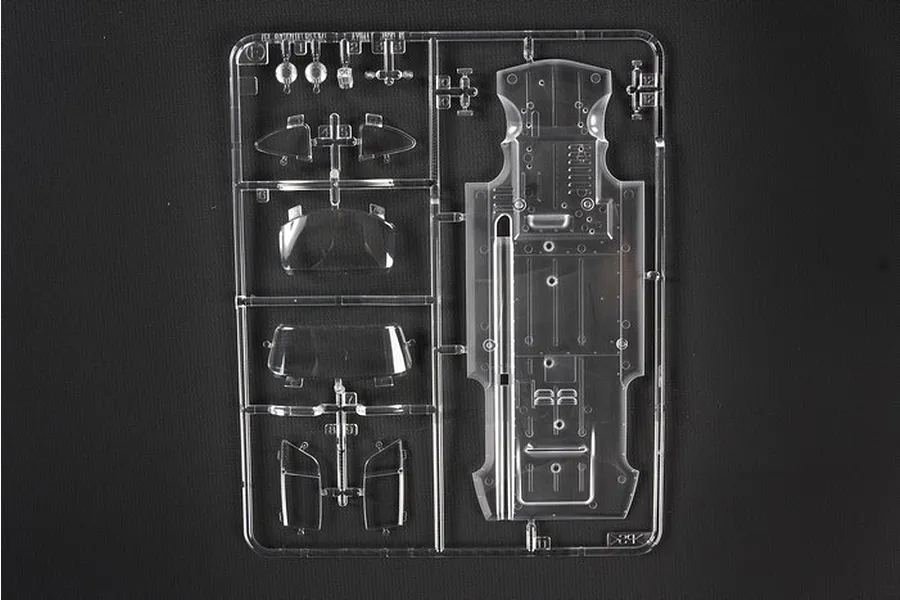 A clear plastic sprue containing various transparent model car parts, including windows and a chassis floor, for a Tamiya 1/24 scale model kit.