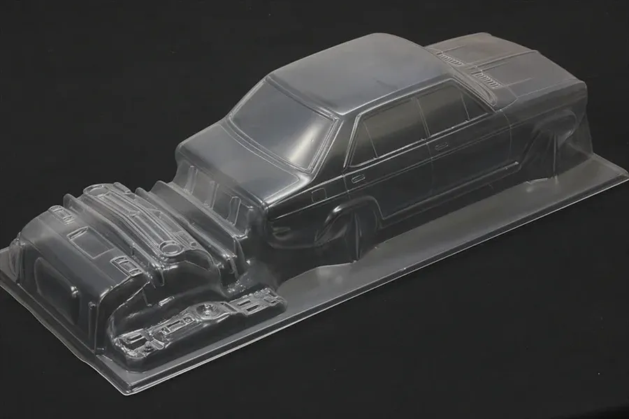 Clear unpainted polycarbonate RC car body shell for a 1/10 scale sedan with separate molded parts on a dark background.