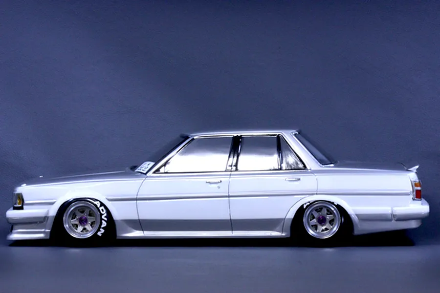 Side profile of a painted white and silver Toyota Cresta GX71 RC drift car body mounted on a chassis with custom wheels against a dark background.