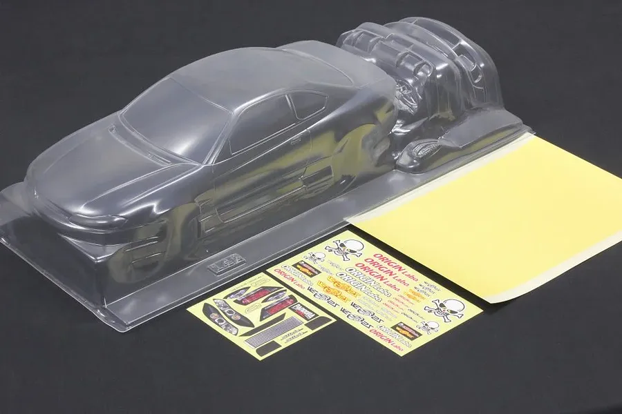 Unpainted clear polycarbonate RC car body shell with separate parts and decal sheets on a dark surface.
