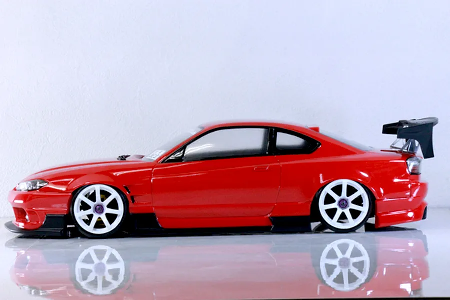 Side profile of a red Pandora RC S13 Silvia radio-controlled drift car body with white multi-spoke wheels, black aero kit, and large rear wing against a plain white background.