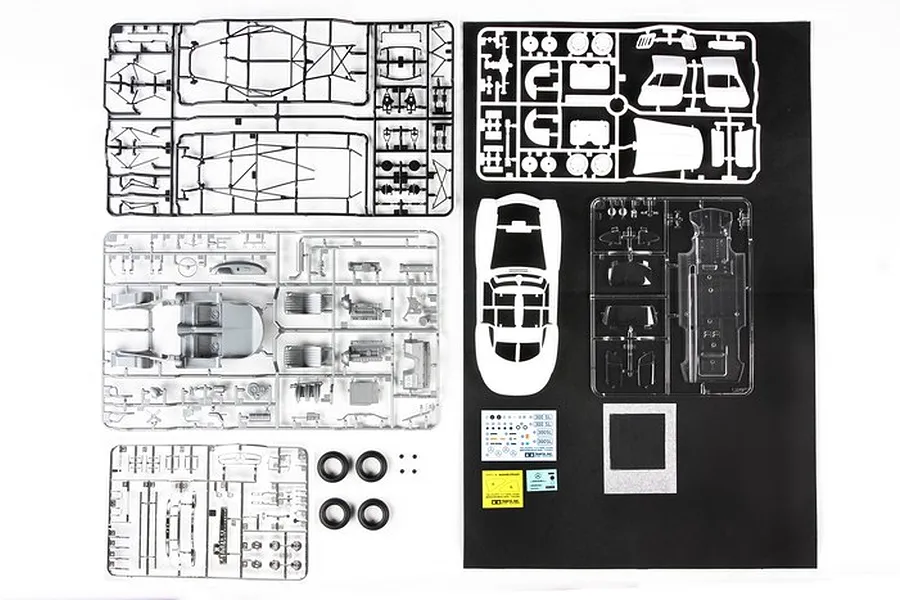 Top-down view of Tamiya 1/24 Mercedes-Benz 300SL model kit parts, including plastic sprues, rubber tires, decals, and body shell on a black background.