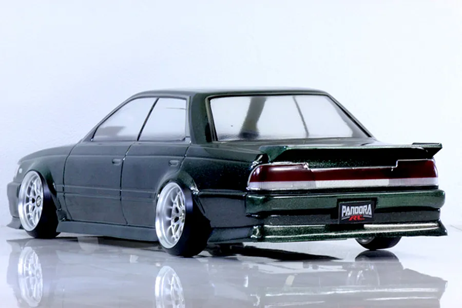 Rear three-quarter view of a dark metallic green RC drift car body shell mounted on a chassis with custom wheels against a white background.
