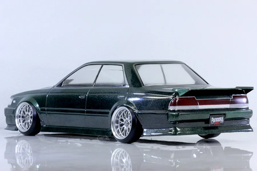 Rear-three-quarter studio shot of a dark green metallic RC drift car body mounted on a chassis with custom wheels against a plain white background.