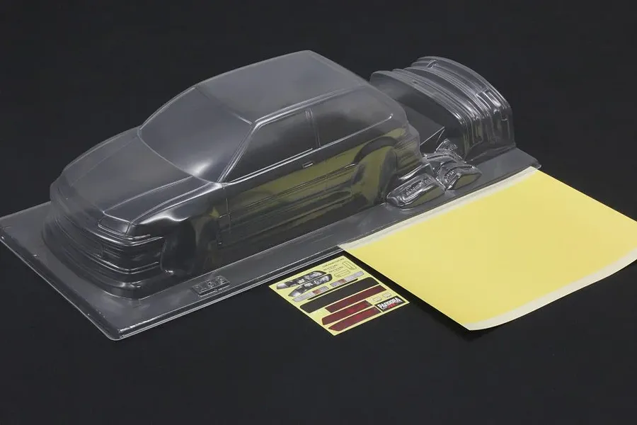 Unpainted clear RC body shell for a Honda Civic EF9 with included mask sheet and decals on a dark surface.