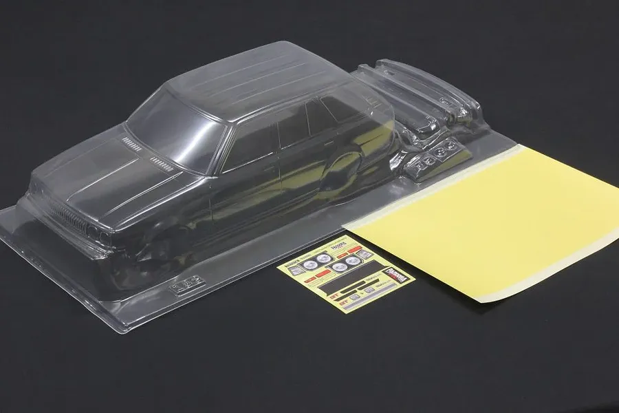 Clear unpainted Pandora RC Toyota Corolla KE70 wagon body shell with masking sheet and decal sheet on black surface.