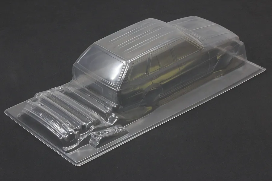 Clear unpainted polycarbonate RC car body shell of a wagon displayed on a dark surface.