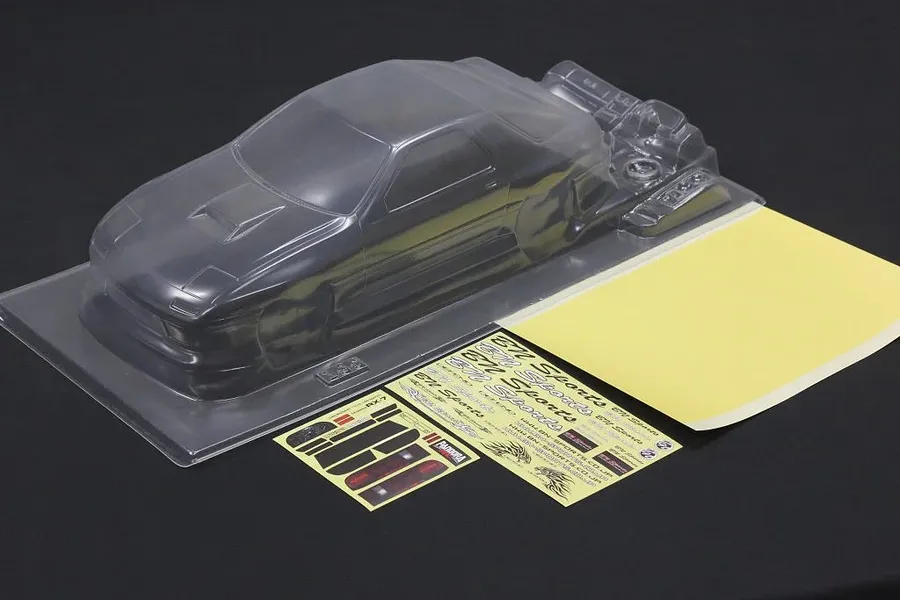 Clear unpainted polycarbonate RC car body shell with separate decal sheets on a dark surface.