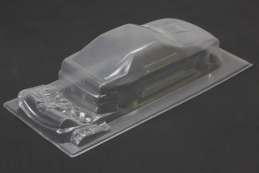 Unpainted clear RC car body shell for a Mazda RX-7 on a dark background, showing molded details and additional parts.