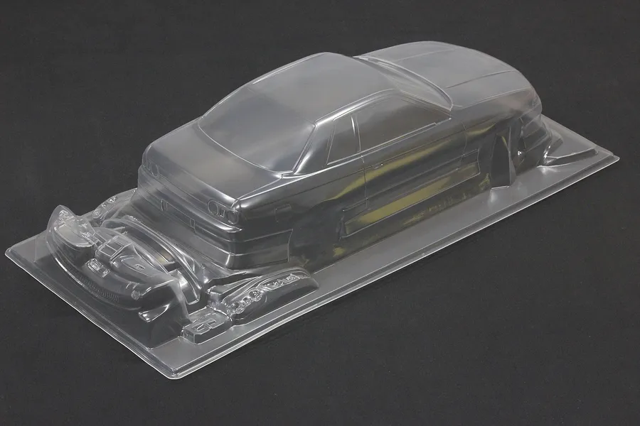 Unpainted clear polycarbonate RC car body shell for a Nissan Skyline R32 2-door with BN Sports styling, shown on a dark background.
