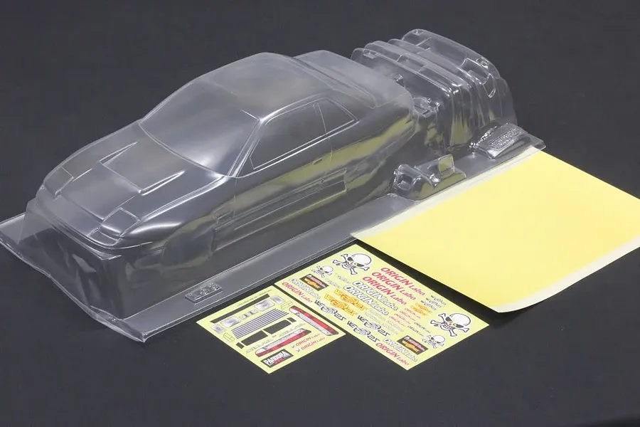 Clear unpainted polycarbonate 1/10 scale RC body shell with separate decal sheets and masking film on a dark surface.