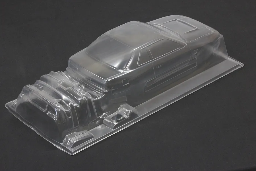 Unpainted clear polycarbonate RC car body shell with additional molded accessory parts on a dark background.