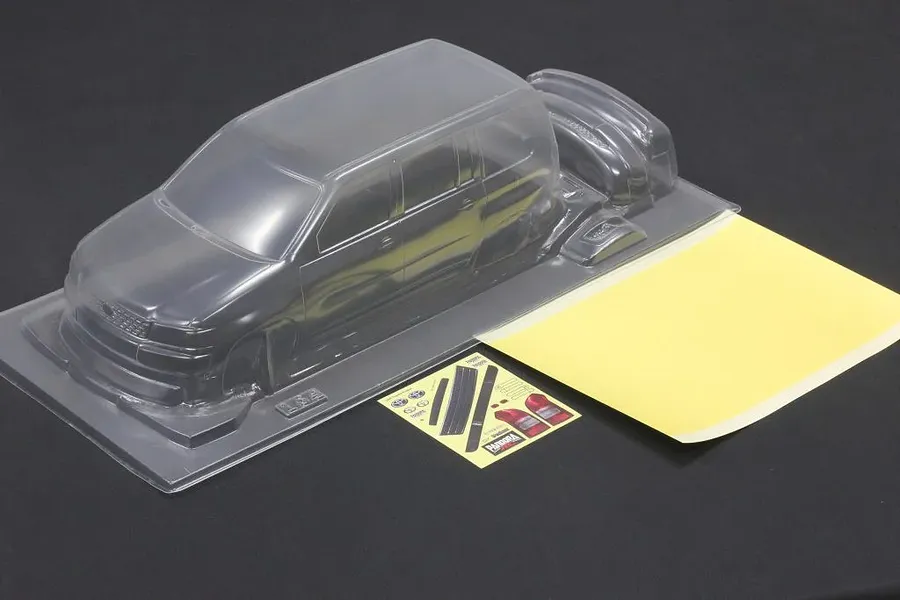 Unpainted clear polycarbonate RC car body shell with window masks and decal sheet on dark surface.