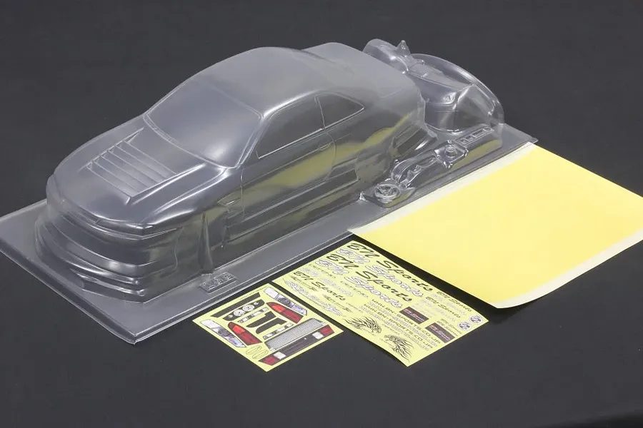 Unpainted clear polycarbonate RC car body shell with separate decal sheets and window masks on a dark surface.