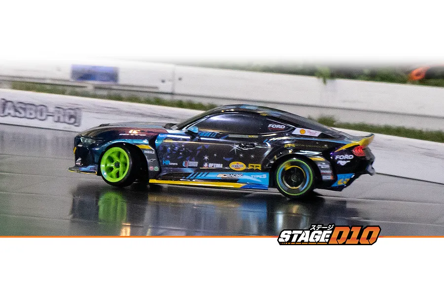 Action shot of the HPI Stage-D10 Ford Mustang GT RC drift car drifting on an indoor RC track with bright green wheels.