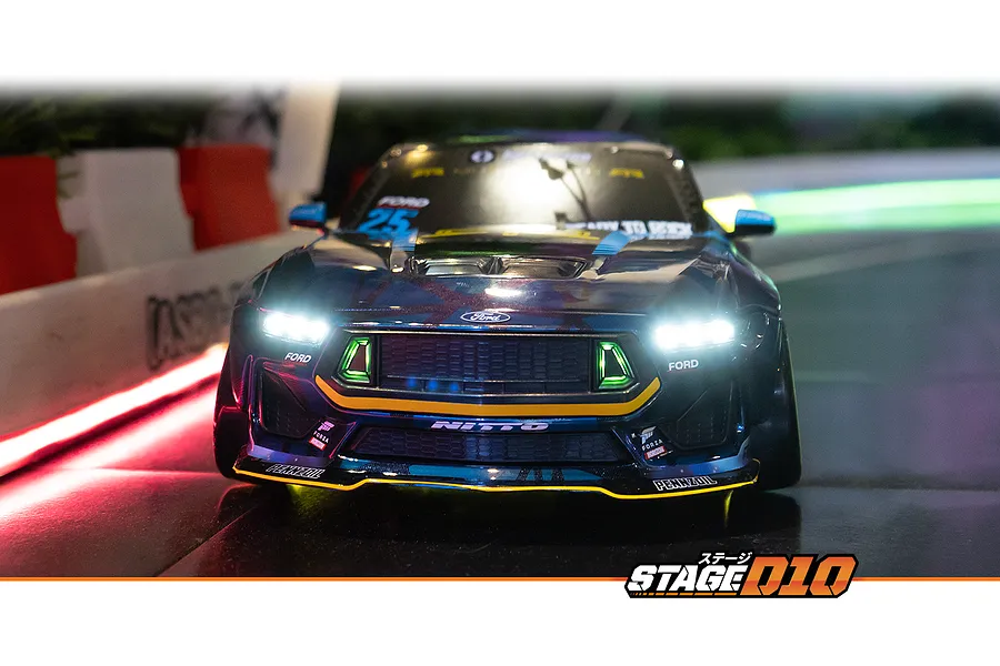 Front view of an HPI Stage-D10 Ford Mustang GT RC drift car with illuminated headlights and grille lights on a track.