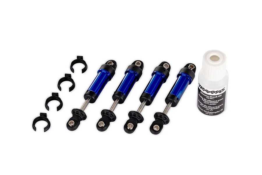 Four blue aluminium RC shock absorbers with black caps and springs spacers, plus a small bottle of silicone shock oil on a white background.