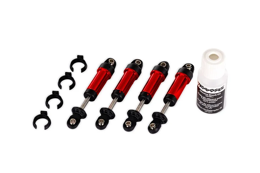 Four red aluminium RC shock absorbers, four black preload spacers, and a bottle of silicone shock oil on a white background.