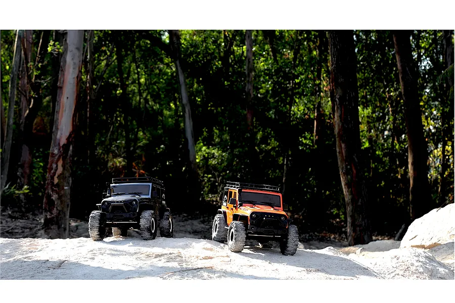 Two 1/10 scale RGT Rock Cruiser RC crawlers, one black and one orange, parked on an outdoor dirt trail surrounded by trees.