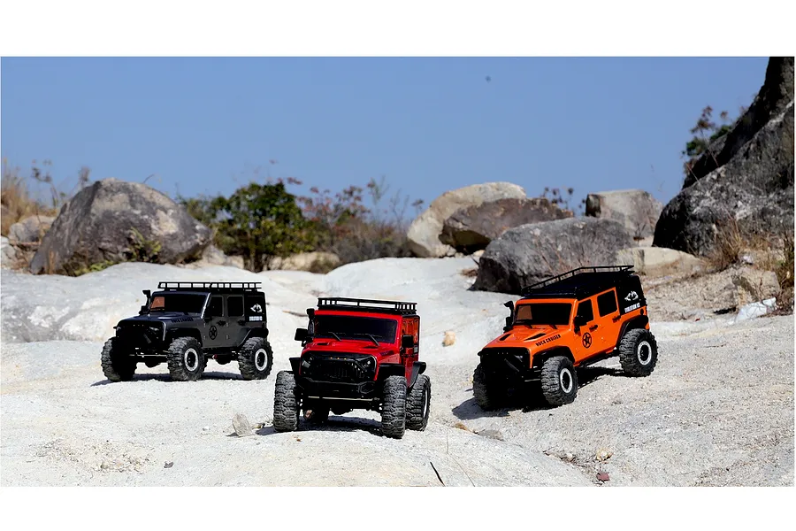 Three RGT Rock Cruiser Evolution V3 1/10 scale RC crawlers in black, red, and orange parked on a rocky outdoor terrain.