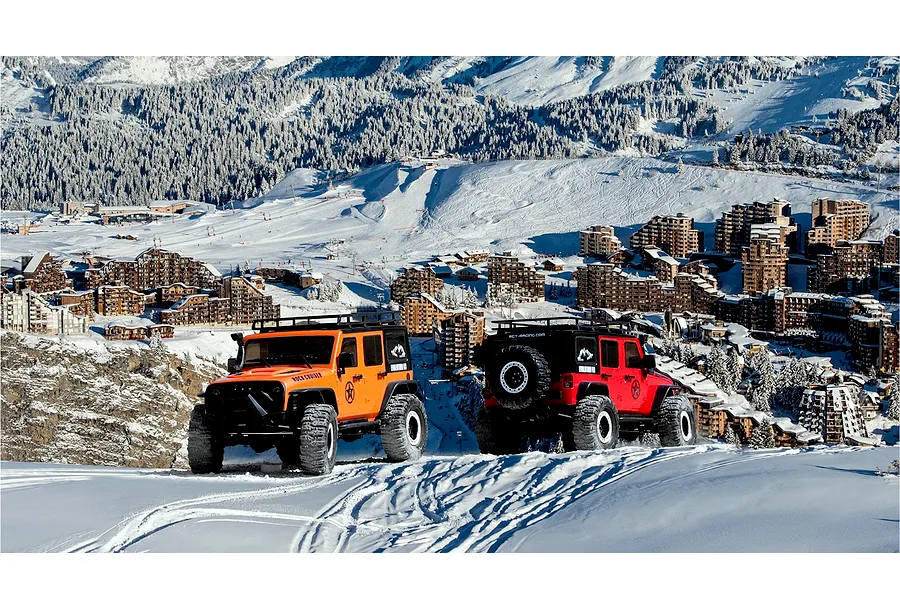 Two 1/10 scale RGT Rock Cruiser RC rock crawlers in orange and red driving on snowy mountain slopes.