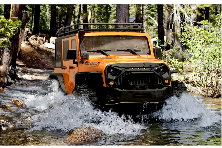 Orange RGT Rock Cruiser RC rock crawler driving through a shallow stream in a forest.