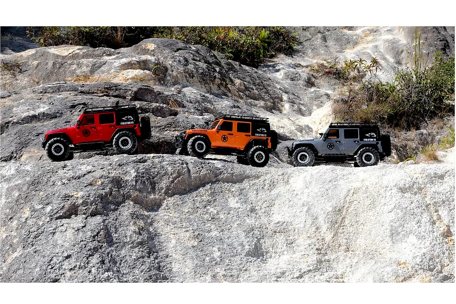 Three RGT Rock Cruiser Evolution V3 RC rock crawler models in red, orange, and grey parked on rocky outdoor terrain.