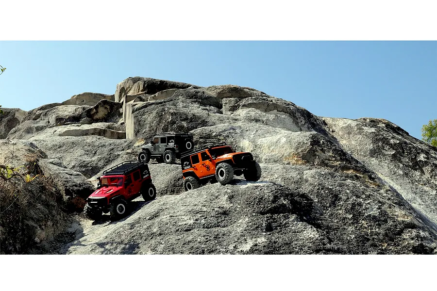 Three RGT Rock Cruiser RC rock crawler models in red, orange, and grey navigating a rocky outdoor terrain.