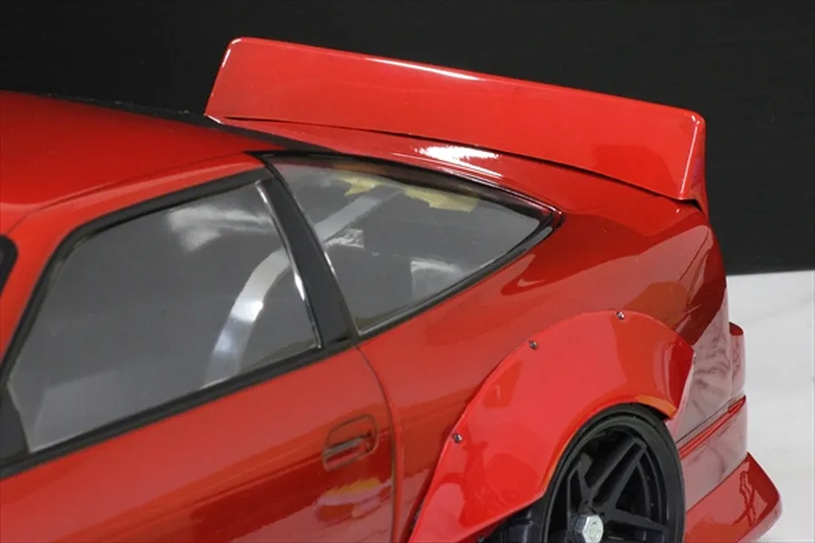 Close-up of a red RC car body featuring a ducktail spoiler mounted on the rear decklid and wide fender flares.