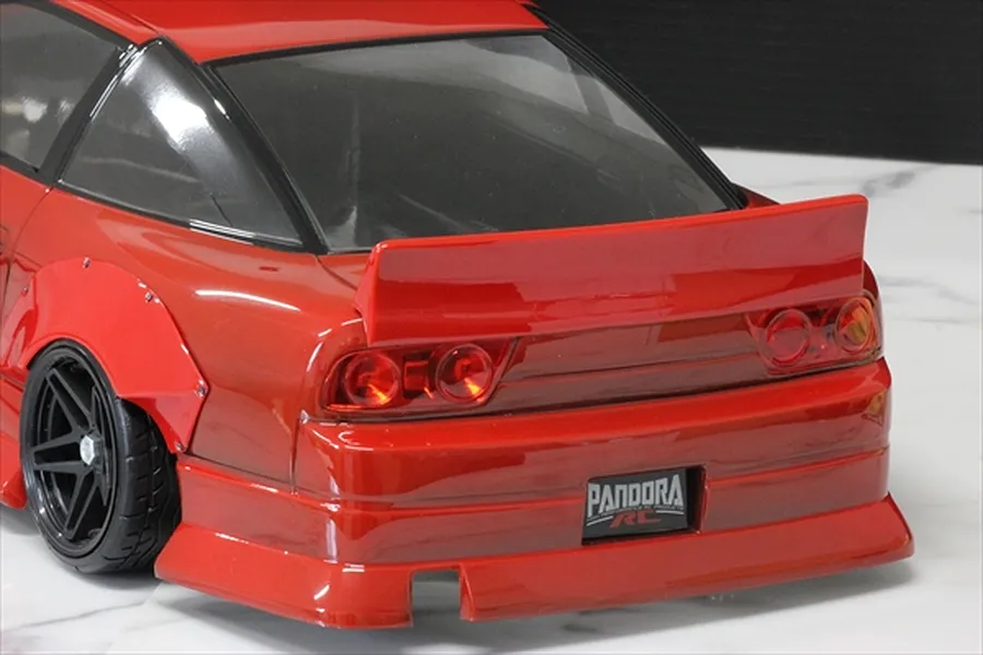 Rear view of a red RC drift car body featuring a ducktail spoiler, wide fender flares, and Pandora RC license plate on a marble surface.
