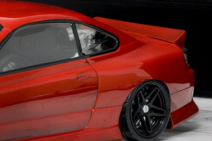 Close-up of the rear quarter section of a red RC drift car model featuring a ducktail spoiler and black multi-spoke wheel.