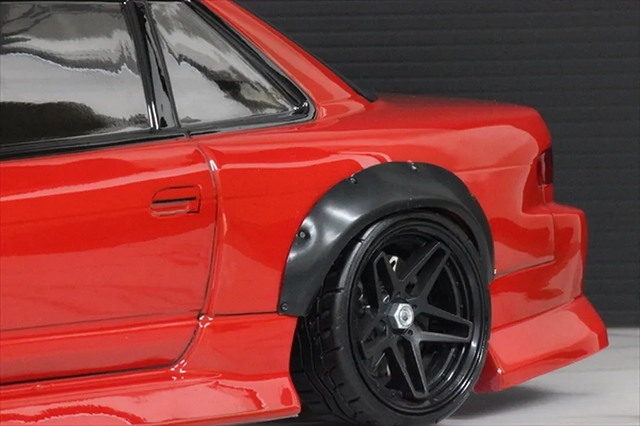 Close-up of a red RC drift car body showing a black over fender installed over the rear wheel arch.