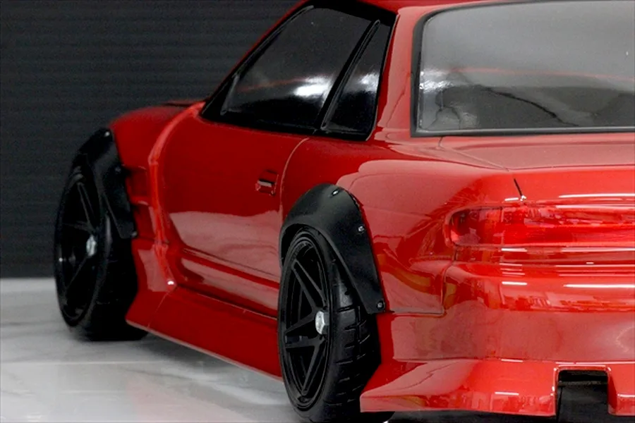 Close-up of a red RC drift car installed with black over fenders and wheels on a smooth studio surface.