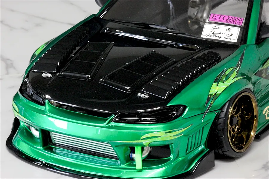 Close-up of a green RC drift car body shell featuring black hood vents and aftermarket duct parts installed on the front end.