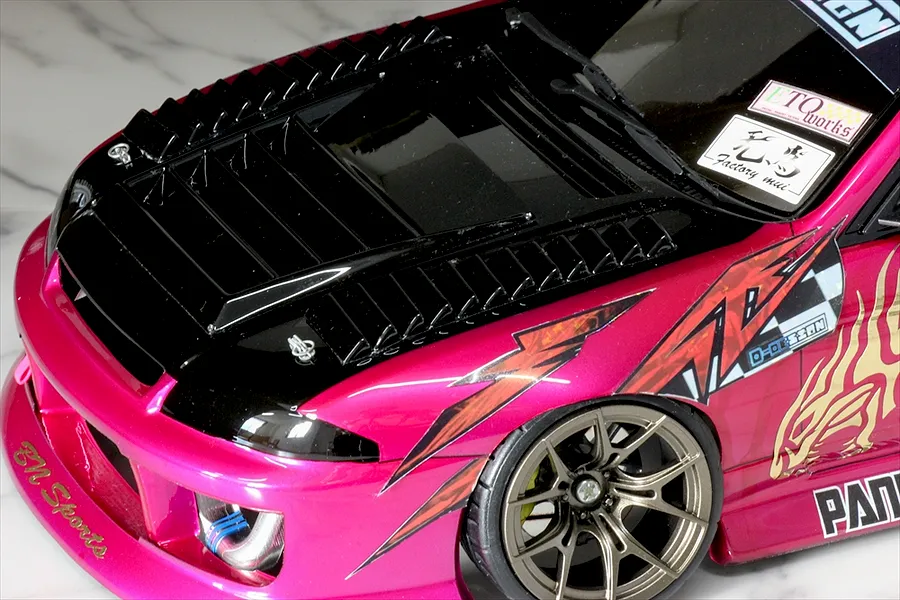 Close-up of an RC car body shell featuring black hood vents, a pink and black painted finish, and custom decals.