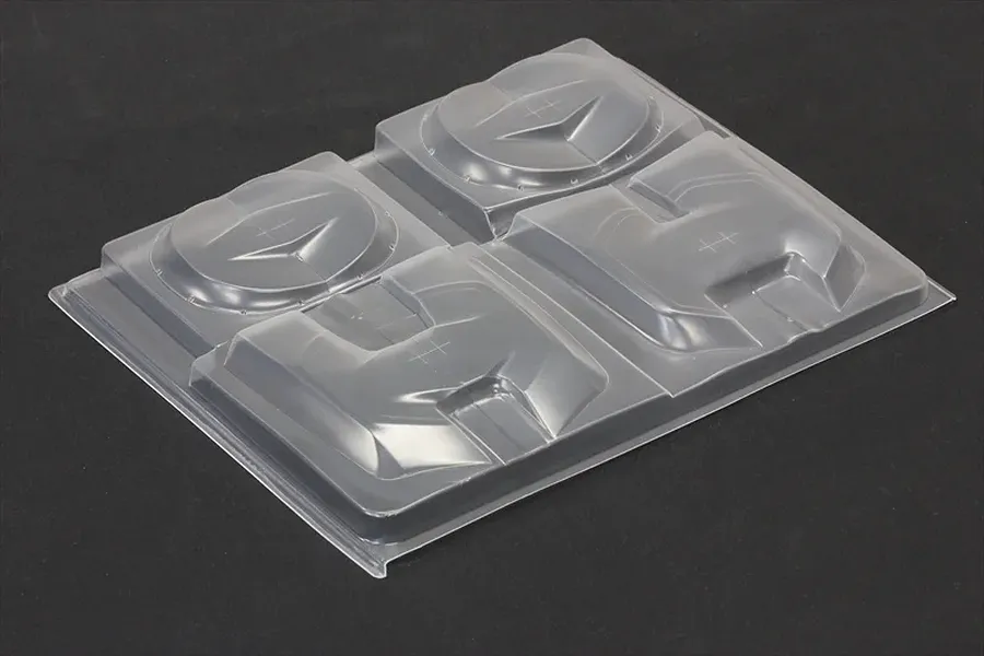 Unpainted clear plastic over fender set sheet for RC body shell on a dark surface.